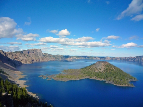 A small island sits in the middle of a vivid blue lake ringed by mountains.