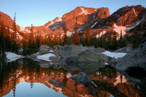 Red-tinged mountains and blue sky reflected at dawn in a lake