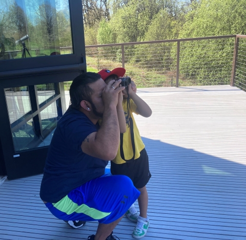 A father and son each look through a pair of binoculars at something in the distance.