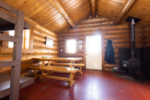 Inside of a log public use cabin with table, woodstove, and bunks.