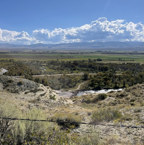 looking down a cliffside to a river in an open valley