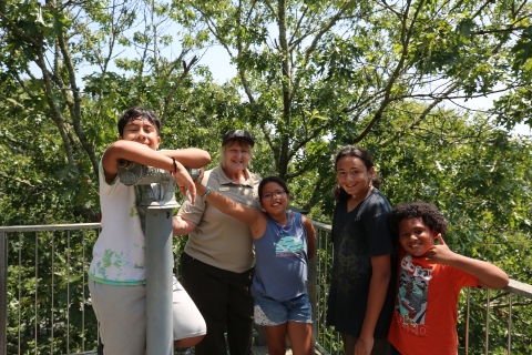 a woman in service uniform smiles with a group of kids surrounded by forest