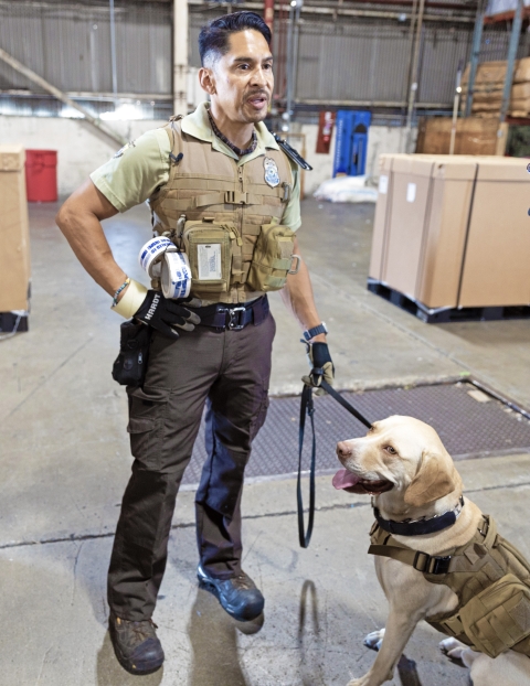 Officer standing with this dog on a leash in a warehouse.