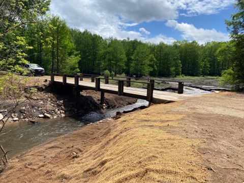 A bridge over a free-flowing creek with burlap covered soil for replanting on the banks