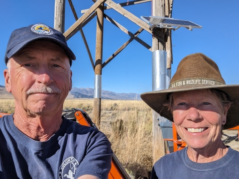 Two people stand together smiling, with desert in the background.