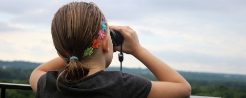 A young woman looking through binoculars along a railing