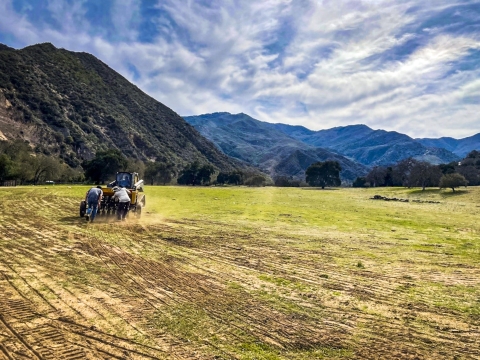 A drill seeder being pushed along a wide open field