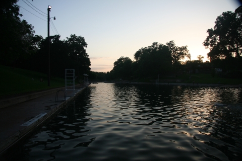 Barton Springs pool is shown against a background of a sunset.