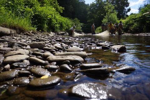 Upclose view of a stream flowing over smooth rocks with people conducting work in the background