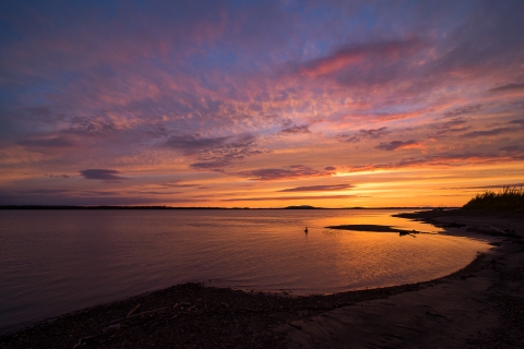 Sunset over a river paints the sky orange and purple.