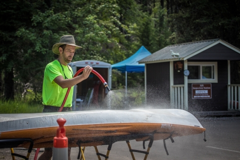 A man uses a hose to wash off the bottom of a kayak