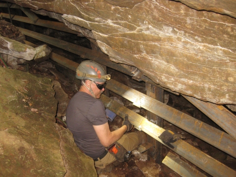 A man in a hard hat builidng a wooden barrier inside a cave.