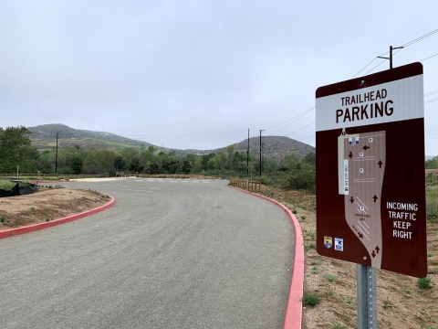 Trailhead parking sign with map on the side of the road entering the refuge parking lot.