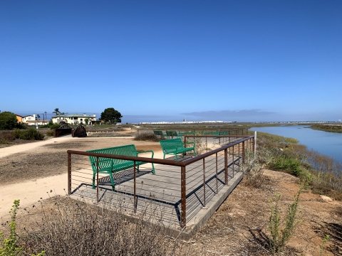 Deck area with green benches near river. 