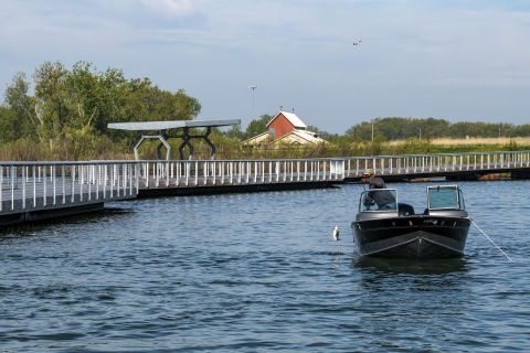 Looking straight at a fishing boat catching a white bass with fishing pier along left side and visitor center in background on a sunny day