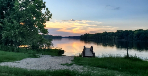 Sunset going down behind clouds over a river with a dock.