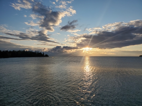 Sun breaking through clouds over a lake.