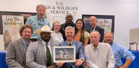 A group of people pose with the winning artwork depicting trumpeter swans.