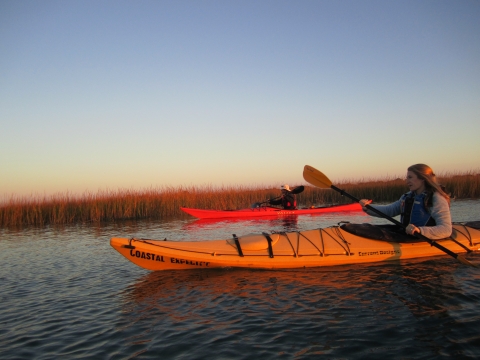 A woman and man paddle kayaks on a late Autumn afternoon in the estuary. 