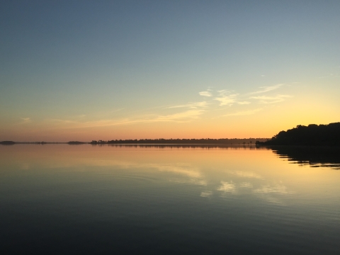 A pastel orange sunset reflects in a placid lake bordered with forest