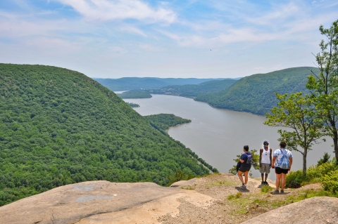 Three people stand on a rocky ledge overlooking a river