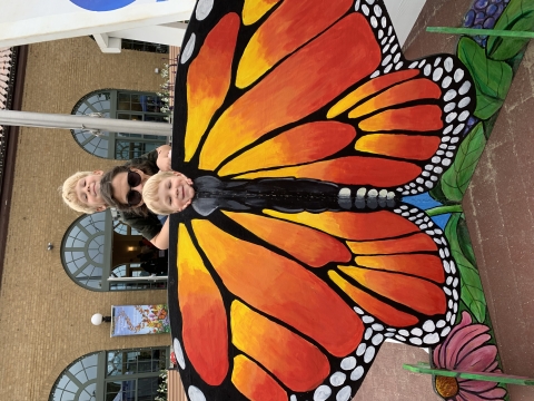 2 small children pose and adult behind a monarch butterfly cutout