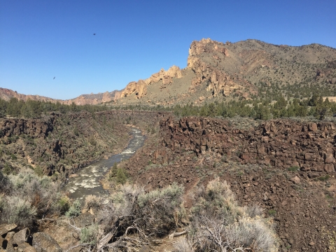 Crooked River snakes its way through the sagebrush and juniper landscape with a rocky mountain (Smith Rock) in the background.