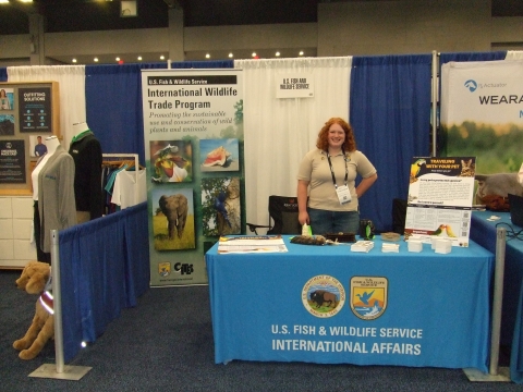 A woman stands behind a table with a tablecloth that reads U.S. Fish and Wildlife Service International Affairs