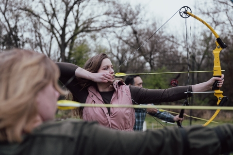 Female archer lines up with other archers and takes aim at target.