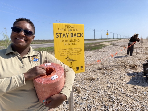 FWS employee smiles at camera and holds a role of twine while another employee uses the twine to build an exclosure to protect nesting birds