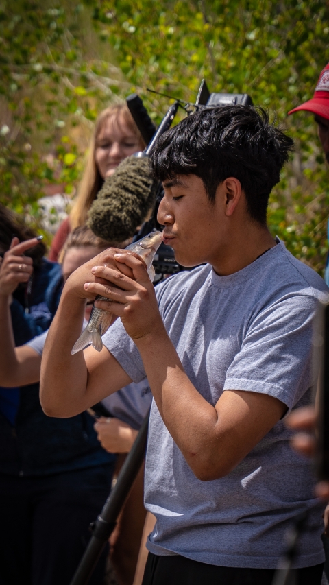 A boy holds a razorback sucker and kisses it before releasing it into the river.