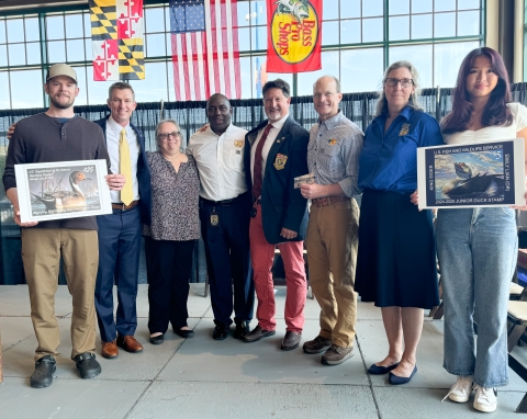 8 people standing, 2 are holding duck stamp art