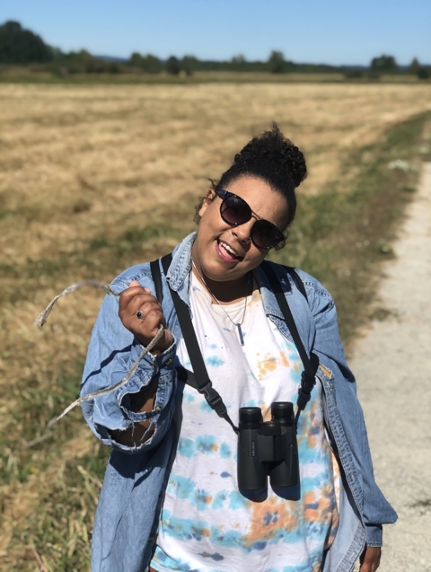 Person outside smiles with sunglasses on and binoculars hanging from neck.