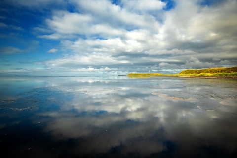 clouds reflect in calm water along coastline