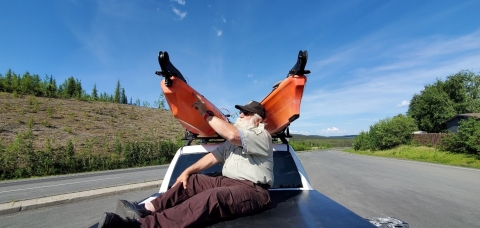 Watercraft inspector physically inspecting two kayaks on top of truck roof rack for aquatic invasive species.