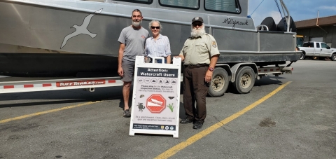 Couple visiting Alaska pose with watercraft inspector at the Alcan Port of Entry.