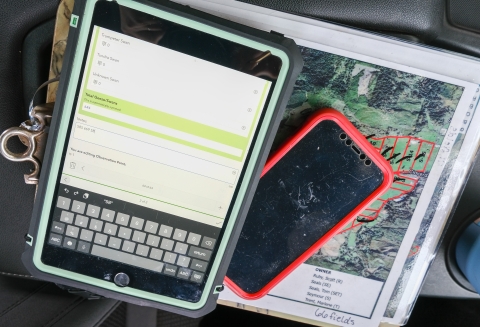 A map, iPad, and iPhone sit on the center console of a truck's front seat.