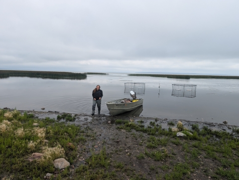 person stands on a lake shoreline with wire traps in the background