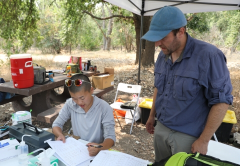 Two people look over data sheets in a outdoor camp setting.