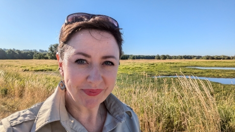 Smiling person with sunglasses on head stands in front of wetlands. 