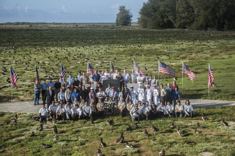 Veterans and Midway Atoll staff pose on field at Midway Atoll surrounding Midway Atoll memorial surrounded by albatross