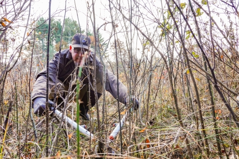 Man kneeling down, using loppers to cut small stems