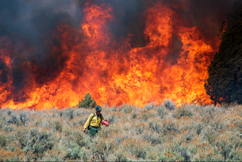 A firefighter walks facing away from a fire burning behind him