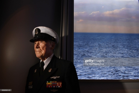 Chief Petty Officer Hank Kudzik poses next to TV screen