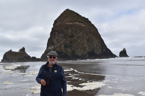 man standing in front of a large haystack rock