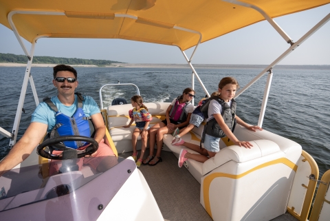 Family wearing lifejackets enjoys a pontoon boat ride on lake. 