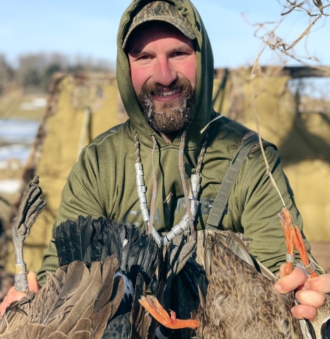 person wears a necklace of bands and holds ducks in hands