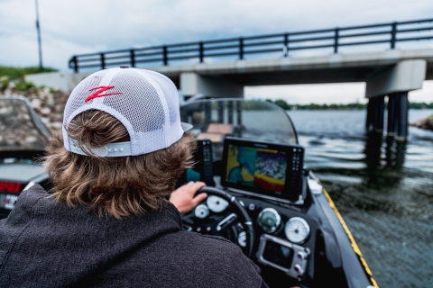 Young man wearing a Z-Man hat pilots fishing boat under a small causeway. 