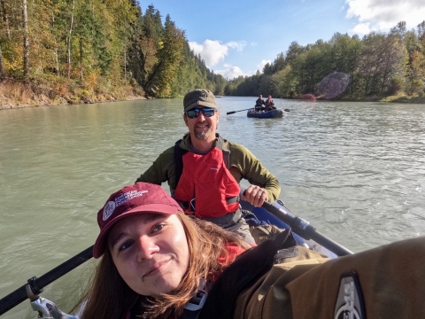 Two service members smile at the camera as they raft down a river. 