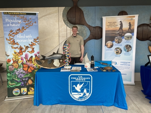 USFWS employee stands behind an outreach table with a invasive carp, DNA strand, turtle shell, and acoustic 